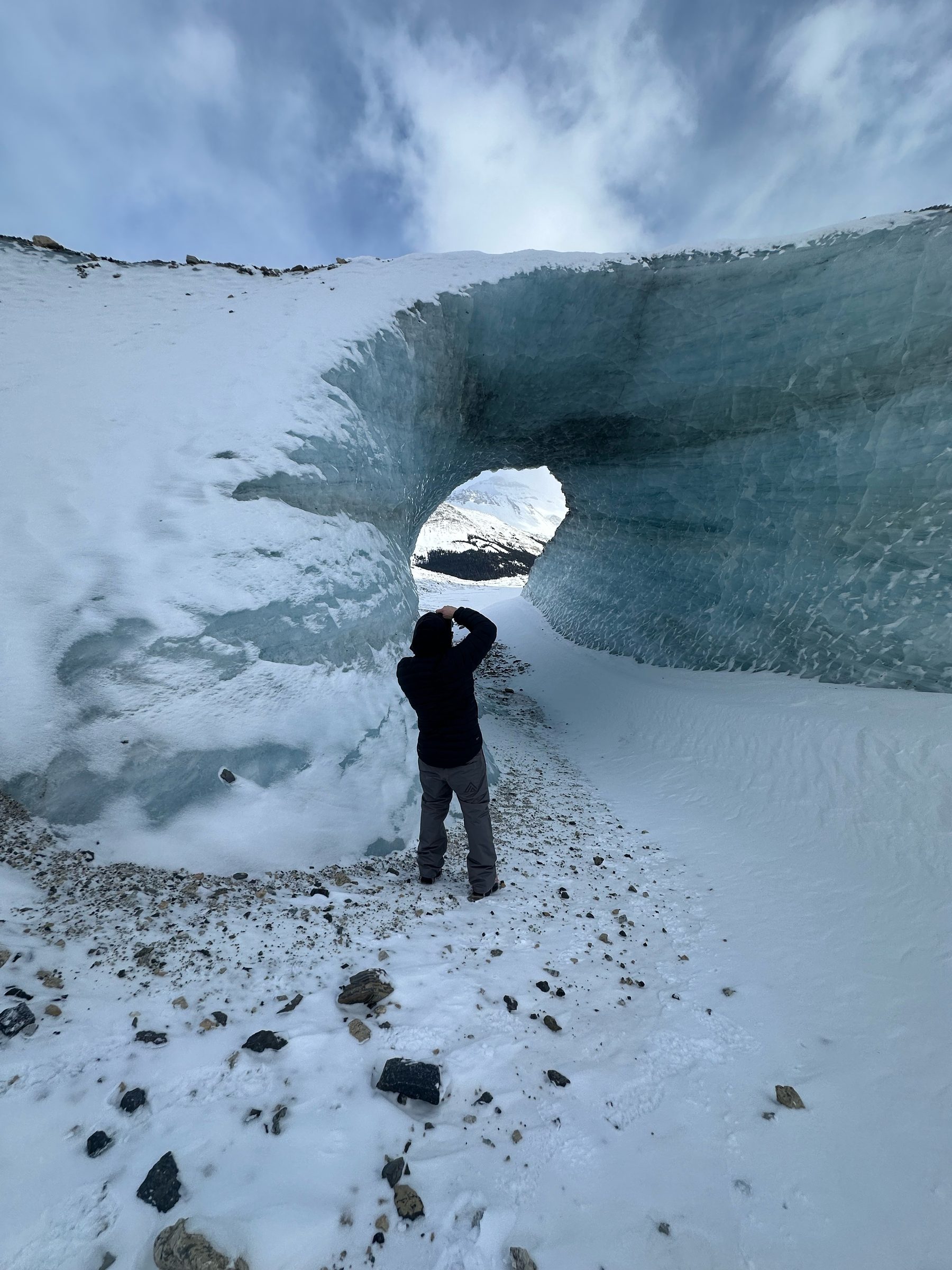 Ryan standing inside the ice arch with a camera raised, photographing the peak through the opening.