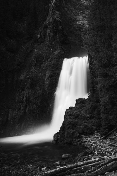 Black and white long exposure waterfall in a dark gorge beside a rock cliff.