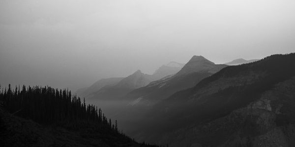 Black and white layered ridges fading into haze with a dark tree covered slope in the lower left.