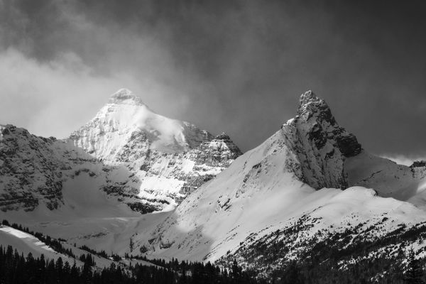 Black and white sunlit snowy peak under a storm sky.