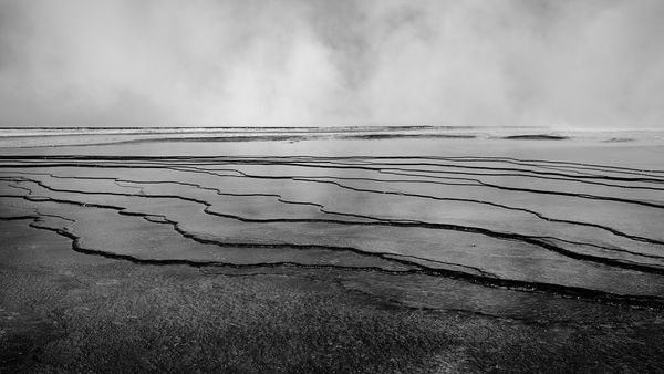 Black and white terraced pools with steam filling the sky.